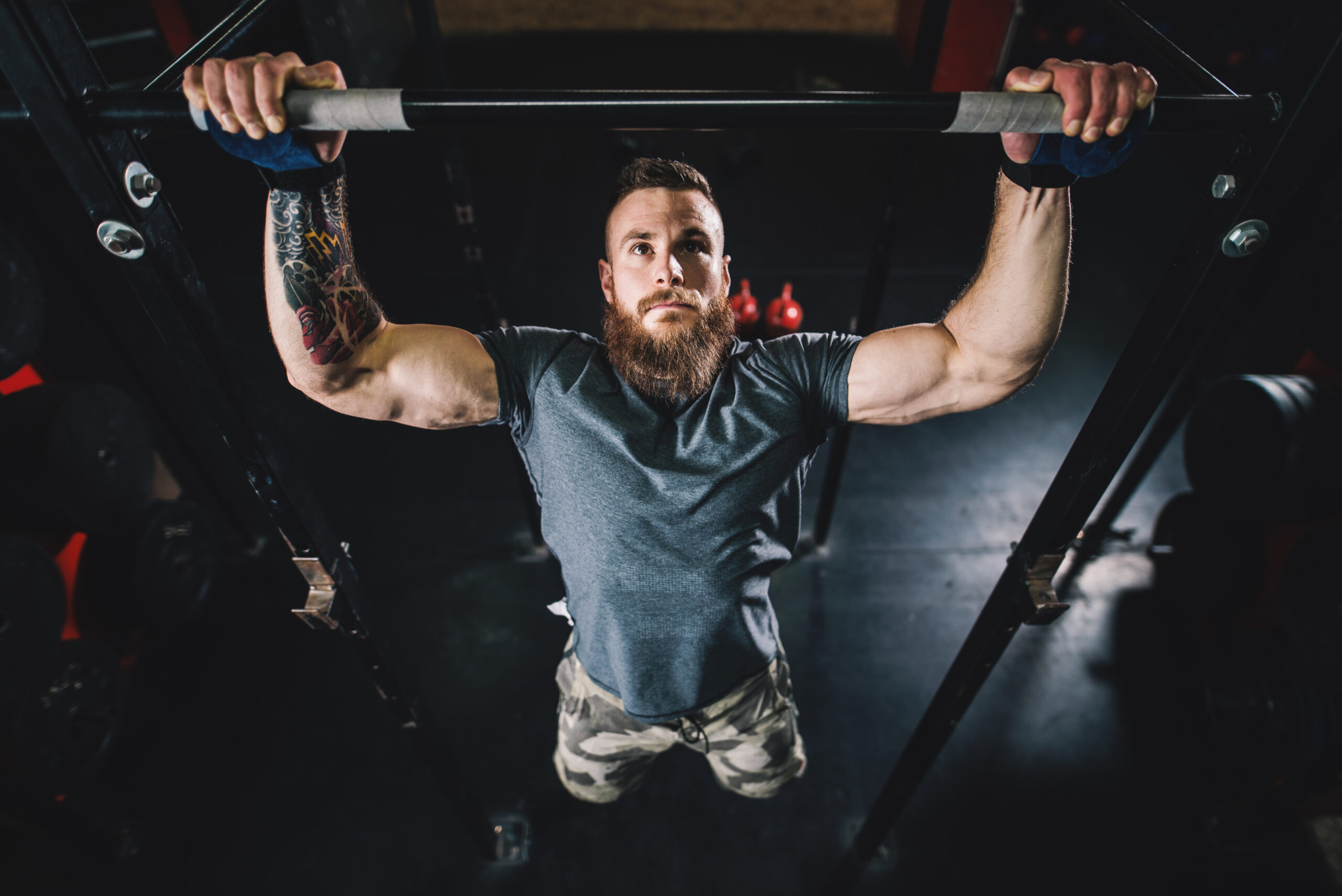 Portrait view of strong active muscular bodybuilder guy doing pull-ups on the bar in the dark modern gym.